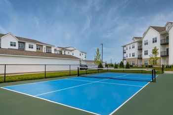 A tennis court is surrounded by apartment buildings.